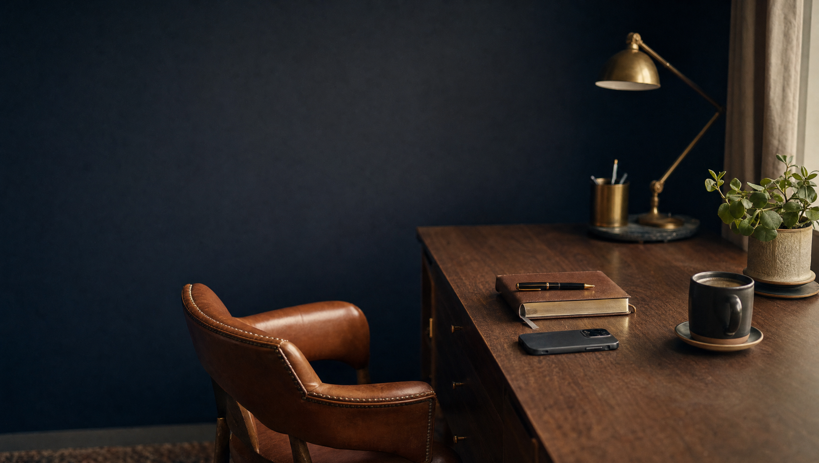 A leather chair pulled up to a desk with a notebook, a phone, and a cup of coffee.